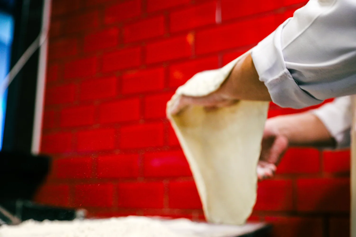 Pizzaiolo stretching dough on a pizzeria make line